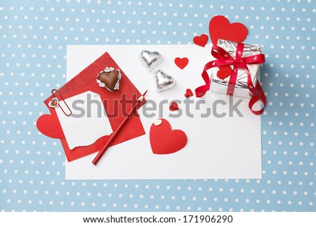 Valentine\'s day love message, unfinished, on white paper with pencil, hearts, gift box with valentine\'s day ribbon and heart-shaped chocolates isolated on blue with white dots background (polka dot)