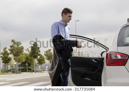 Young business man taking off his jacket and getting into his car - view from behind