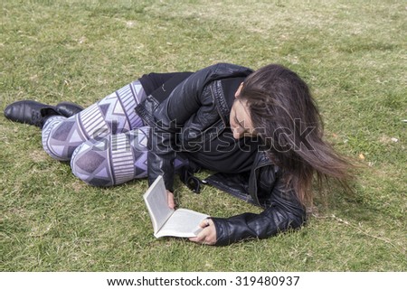 Teenage girl sitting on the grass, reading a book, hair to the wind