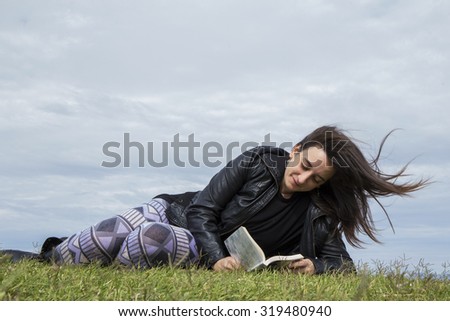 Teenage girl sitting on the grass, reading a book, hair to the wind