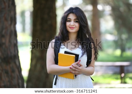 Looking to camera, student girl outdoors, with bag on backside, notebook on hand, exercise book, drawing block, beautiful student girl, young beautiful model, tajik girl