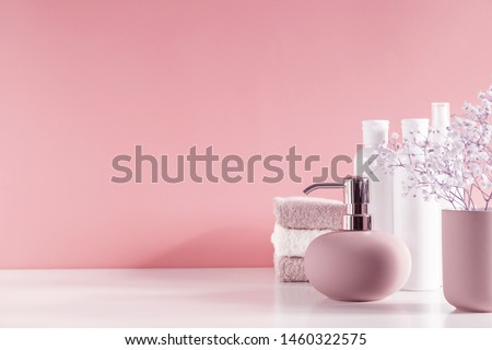 Soft light bathroom decor in pastel pink color, towel, soap dispenser, white flowers, accessories on pastel pink shelf. Elegant decor bathroom interior.