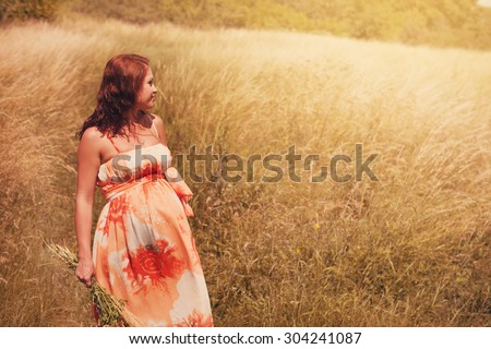 a pregnant woman in the last stages walking in a field of wheat ears in summer afternoon