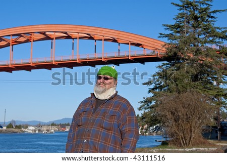 This humorous photo shows an older man in a neck brace and frog hat with an orange bridge and ocean channel in the background.