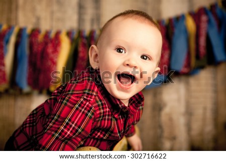 A six month old baby boy smiling on a wood background.