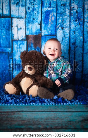 An adorable baby boy posing on a blue background with a teddy bear.