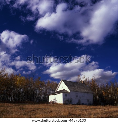 An old prairie school house sits under a cloudy sky in the fall.