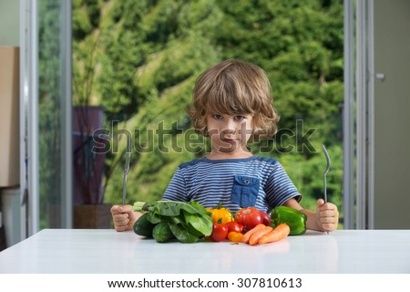 Cute little boy sitting at the table, frowning over vegetable meal, bad eating habits, nutrition and healthy eating concept