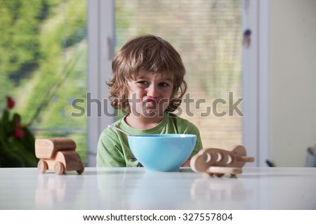Cute little boy frowning over his meal while playing with toys. Bad behavior,  eating habbits concept