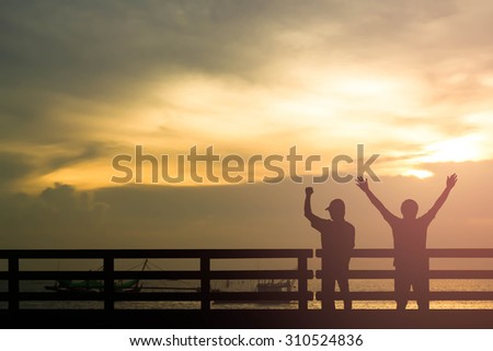 Silhouette successful man or winner man on over blur Beautiful evening sunset above the sea and  boat