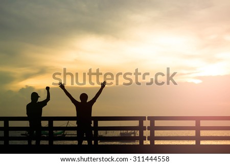 Silhouette successful man or winner man on over blur Beautiful evening sunset above the sea and boat background