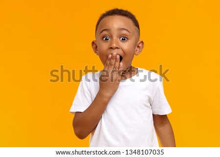 Wow. Studio shot of emotional adorable African American little boy raising eyebrows and covering open mouth with hand being surprised and shocked, showing true astonished reaction on unexpected news Stockfoto © 