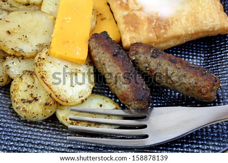 A close view of a fork, fried white potatoes, cheddar and salami cheese slices and pastry on a blue plate.