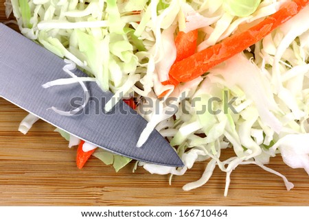 A close view of freshly fine strips of green cabbage with  slices of fresh carrot sticks and  knife on cutting board.