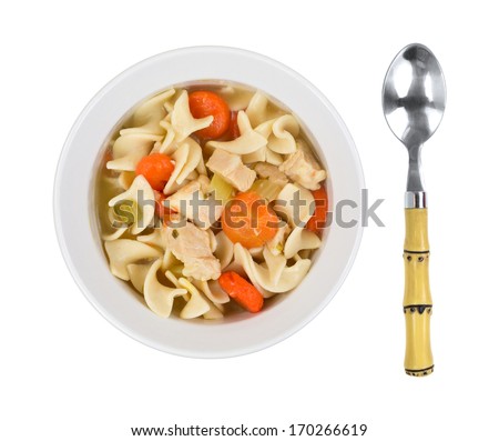 A top view of prepared noodle soup, chicken chunks, carrots in light bowl  with spoon on a white background.