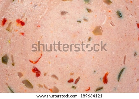 A close view of a bologna slice with bits of pickles and red peppers.