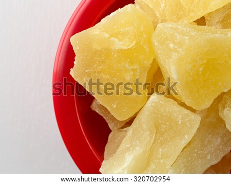 A close view of a red bowl filled with pineapple chunks on a white cutting board.
