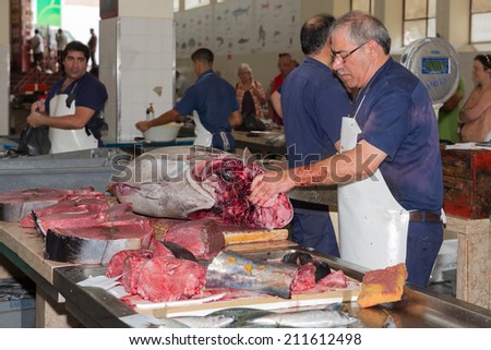 FUNCHAL, PORTUGAL - AUG 01: Butcher preparing a tuna at the fish market of the famous Mercado dos Lavradores on August 01, 2014 in Funchal, capital city of Madeira, Portugal