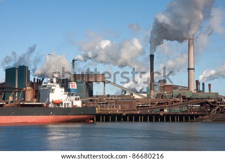 Steel factory with smokestacks and a big cargo ship in front of it