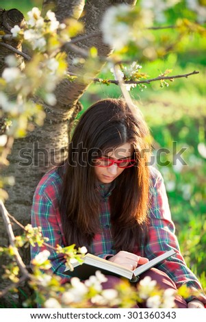 Portrait of a beautiful brunette women with book in blossom apple tree garden in spring time on sunset.