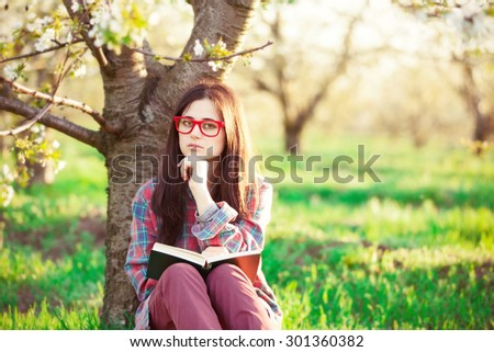 Portrait of a beautiful brunette women with book in blossom apple tree garden in spring time on sunset.