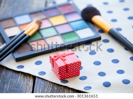 Gift box and brushes for makeup with palette on wooden table.