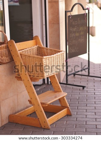 Stand with a wicker basket for vegetables and fruit. In background is a sign with daily offer written in czech language (offer consists of meat and common bakery products).