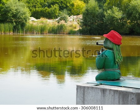 Green water sprite with a pipe and a red hat sitting on the edge of a pond