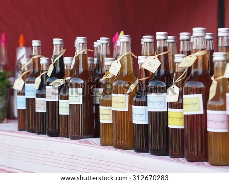 Group of glass bottles with premium herb and fruit syrups. On each bottle is the price tag with the price in Czech crowns and description of the contents (the focus is on the dandelion syrup).