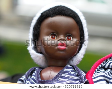 Little black color doll looking wide eyes open in white fut hat.