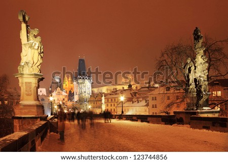 The night View on snowy Prague Lesser Town with Statues on Charles Bridge, St. Nicholas\' Cathedral, Bridge Tower and gothic Castle, Czech Republic