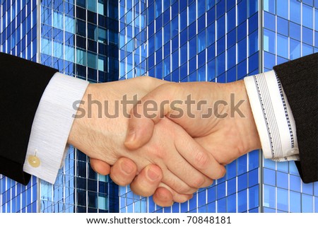 Businessmen shaking hands in front of the Skyscraper on the blue Sky