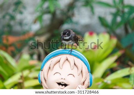 Fantail bird standing on the smiling clay doll.