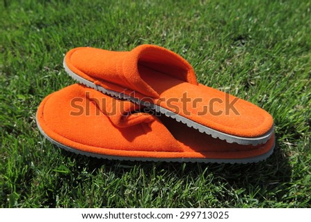 Orange house slippers on mown lawn grass in the summer garden