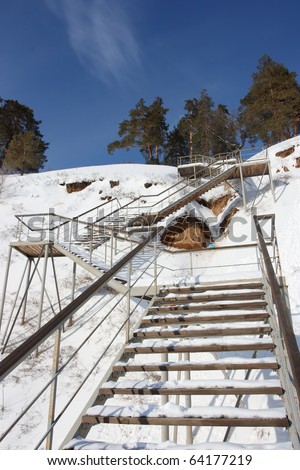 Stairs with landing against a snow slope against pines and a blue sky