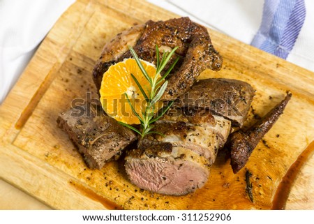 Slices of duck breast with rosemary and slice of orange on wooden cutting board