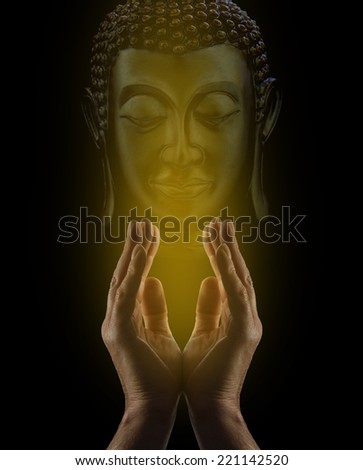 Praying to Buddha - Male healer\'s hands reaching upwards with golden light rising and illuminating a Buddha statue\'s face behind on a black background