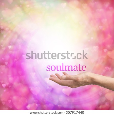 Seeking a soulmate - female hand palm up with the word soulmate floating above, surrounded by a spiral of pastel colored soft focus love hearts on a bokeh background