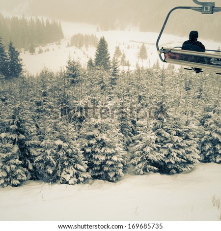 winter mountain resort scene with sportsman silhouette on ski lift over forest landscape