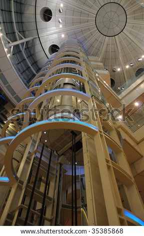 futuristic giant glass elevator going up inside of huge public building