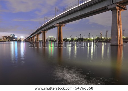 big railway bridge on the tall concrete columns over Tokyo Bay waters by night time