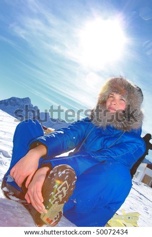beautiful young woman sitting in the snow and smiles. against the sun