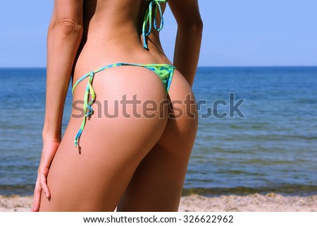 Sexy buttocks with drops of water of a young beautiful sporty woman in bikini posing on the beach after swimming on sunny summer day