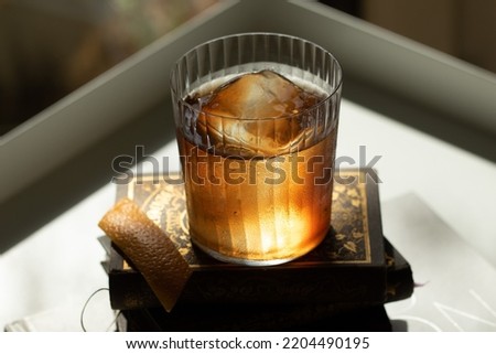Moody shot of an old fashioned cocktail with clear ice cube on vintage books 商業照片 © 