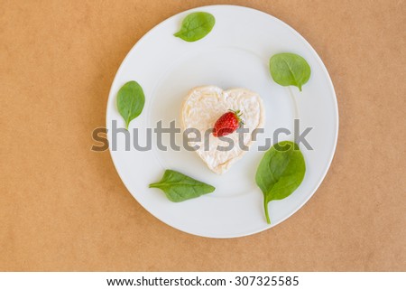 Strawberry on heart-shaped cheese and lettuce on a white plate