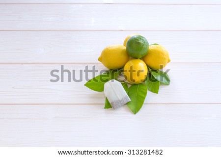 yellow lemons in the form of a pyramid and lime green leaves on top with lemon and tea bag on a white wooden background