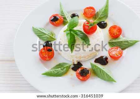 a round piece of cheese with basil and cherry tomatoes on a white plate