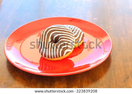 two donuts with sweet zebra coloring on a red plate on a wooden dining table. top view.