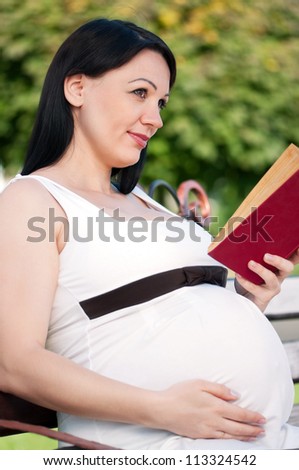 Happy pregnant woman with book in park outdoors