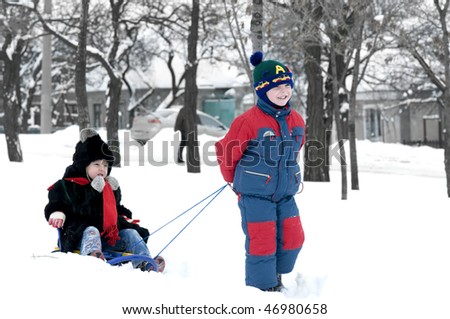 Brother pulling sister on sledge, bright and white winter scene